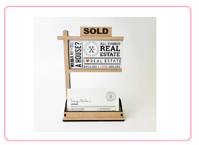 A small wooden real estate sign holder with a "SOLD" sign on top, displaying a business card.